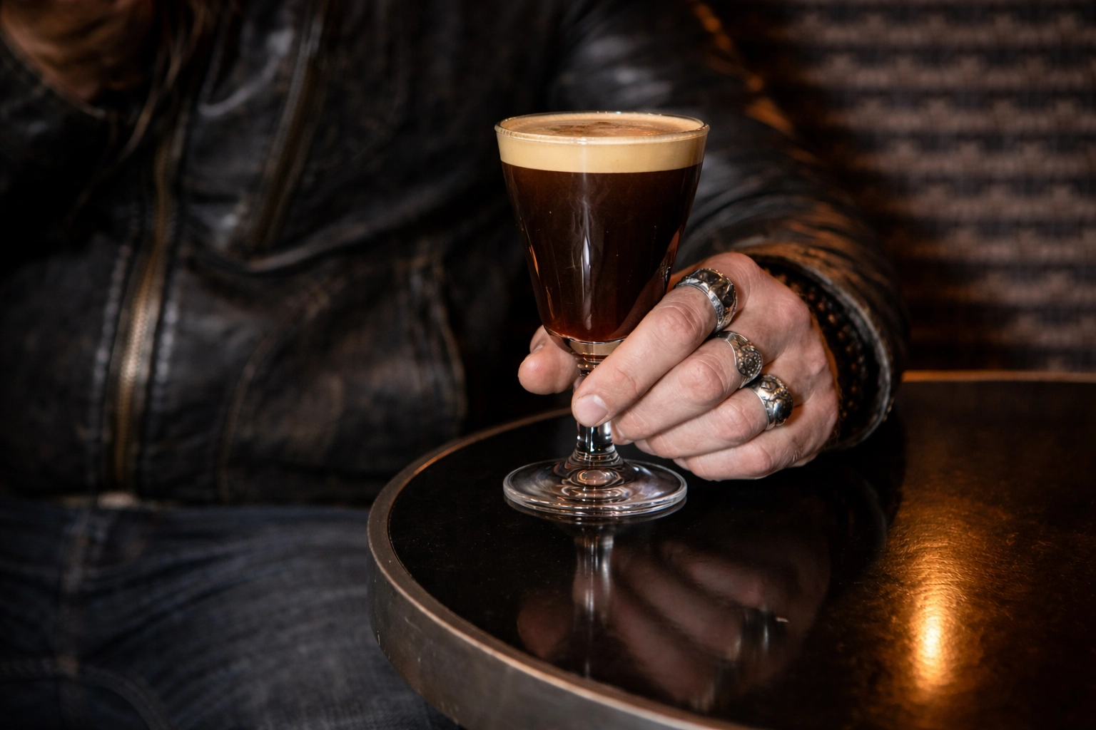 Ringed hand holding an Irish coffee in a Soho bar